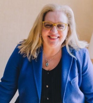Elissa Abreu Smiling woman with long blonde hair, wearing glasses and a blue blazer.