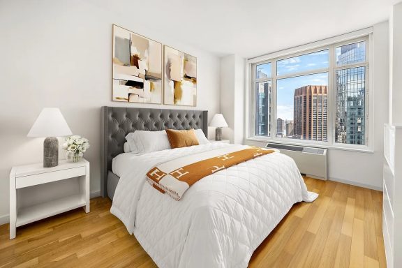 Master bedroom Cozy bedroom with a gray tufted headboard, white bedding, and large window views of the city.