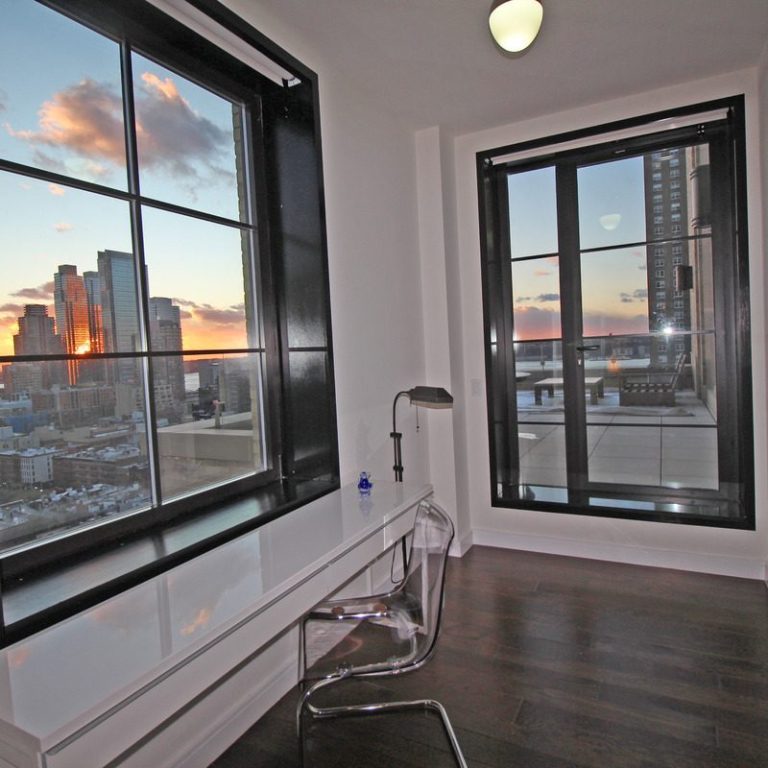 Corner office at 425 West 50th Street Modern office space with a desk and large windows showcasing a city skyline at sunset.